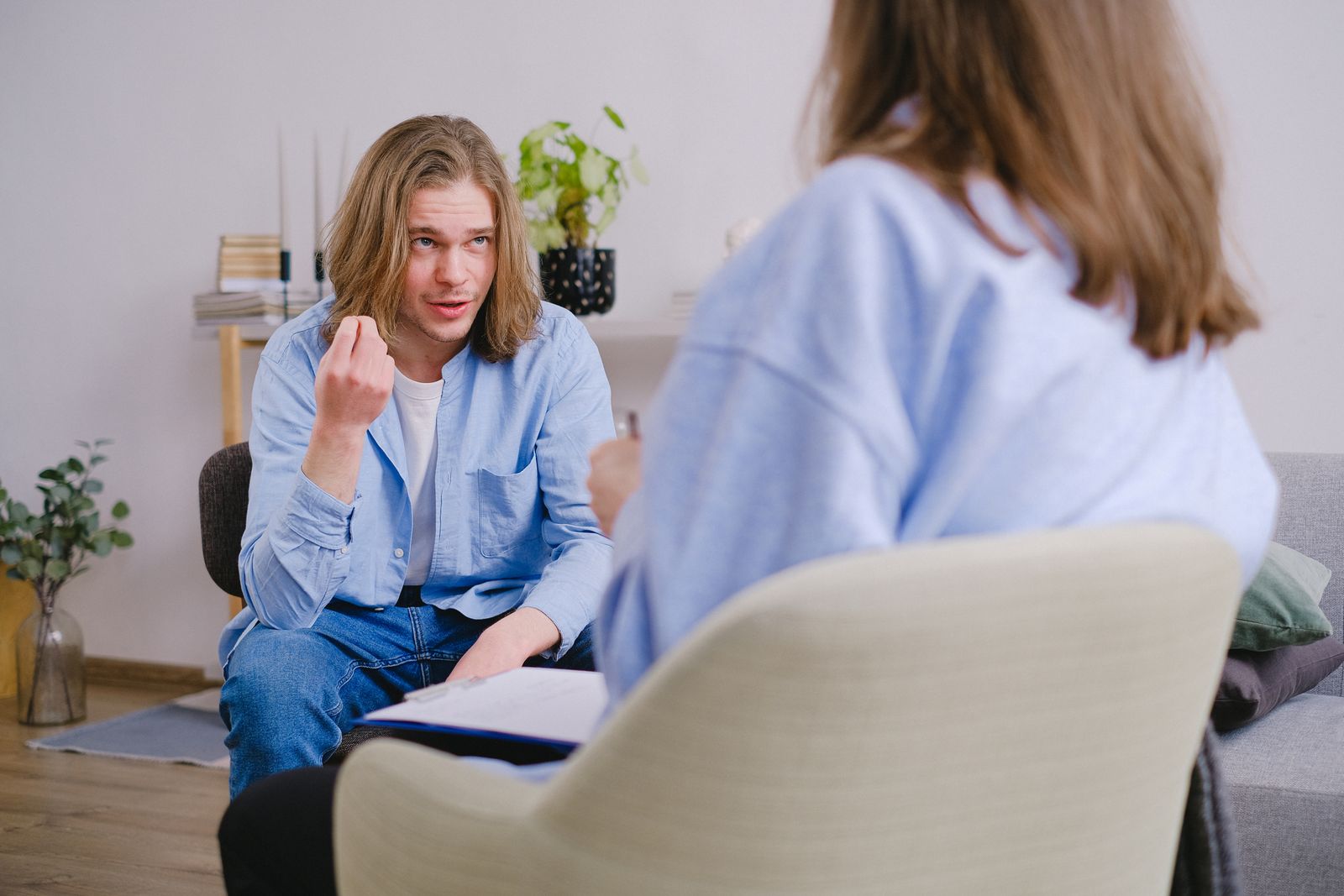 A young man in therapy, gesturing towards therapist in a comfortable setting.