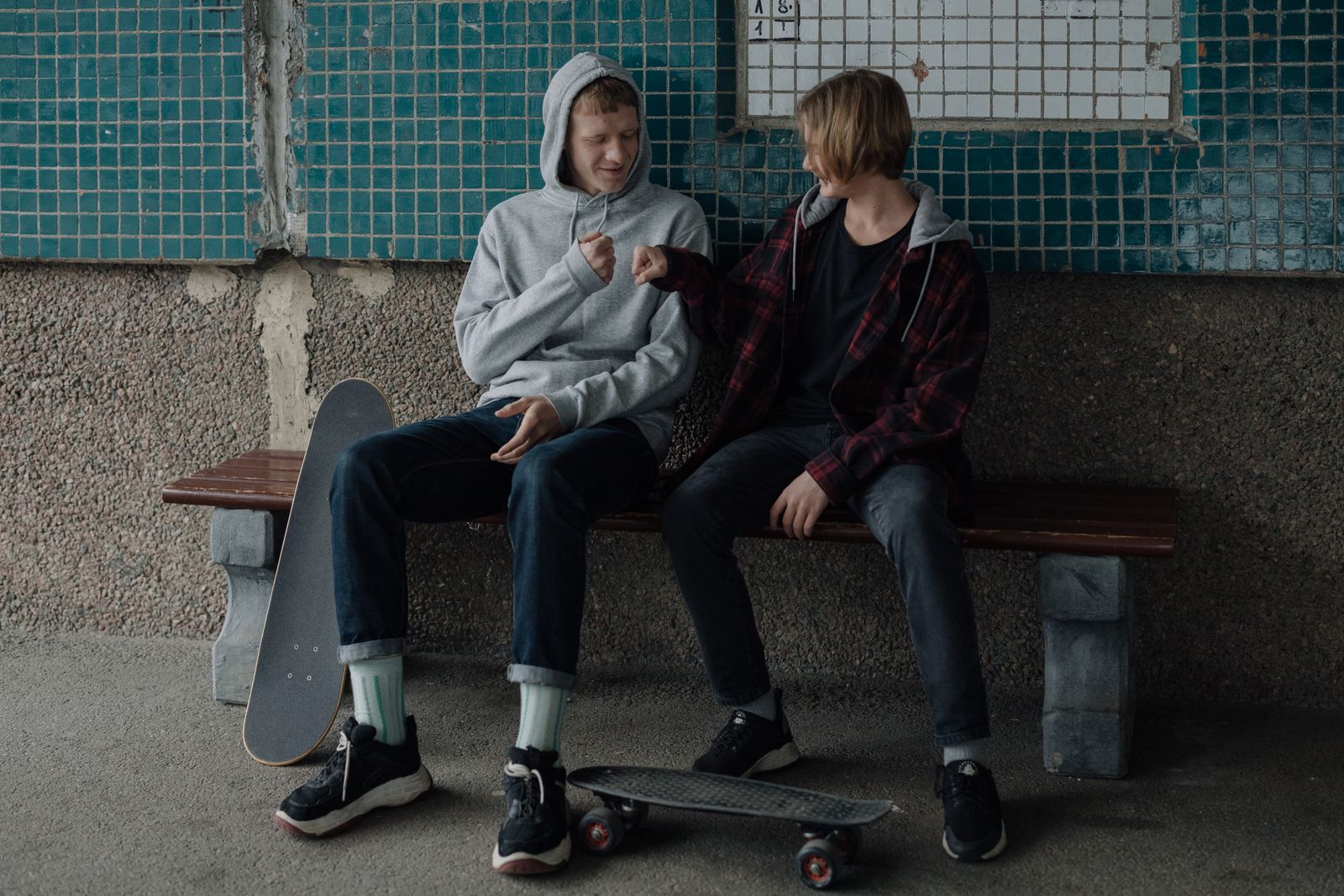 Two teenage friends share a moment on a bench with skateboards, embracing friendship and youth culture.
