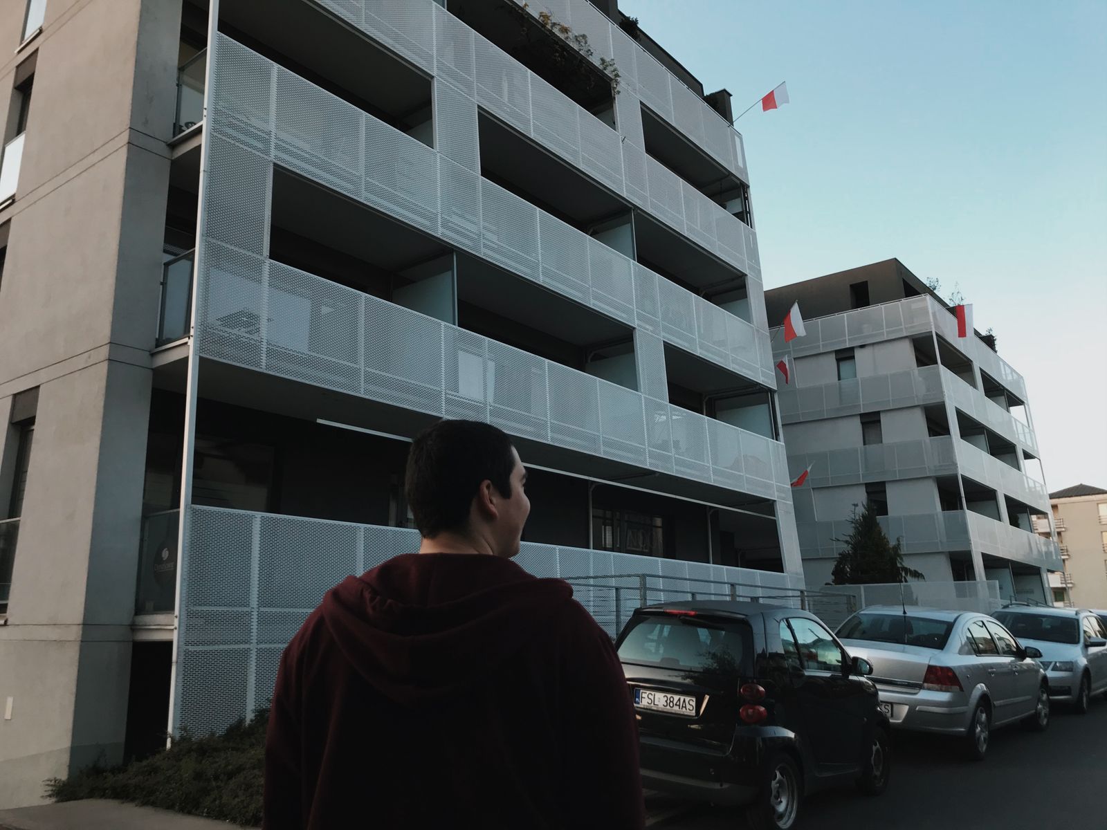 A street scene in Poznań featuring modern apartments, cars, and a person walking.