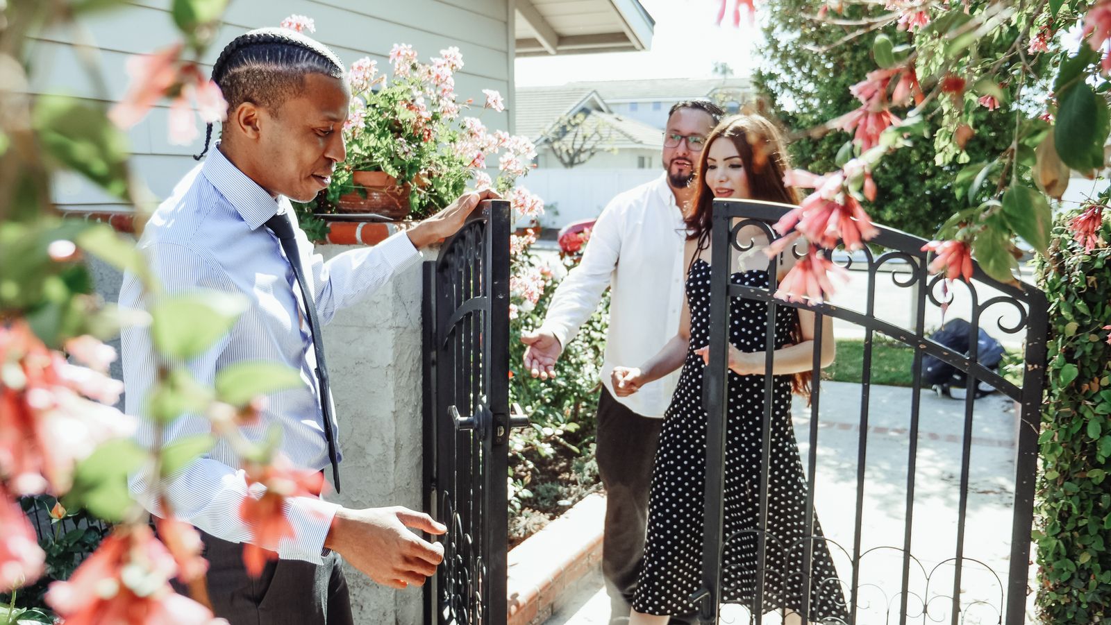 Realtor welcoming a couple to a new house, showcasing the property gate and garden.
