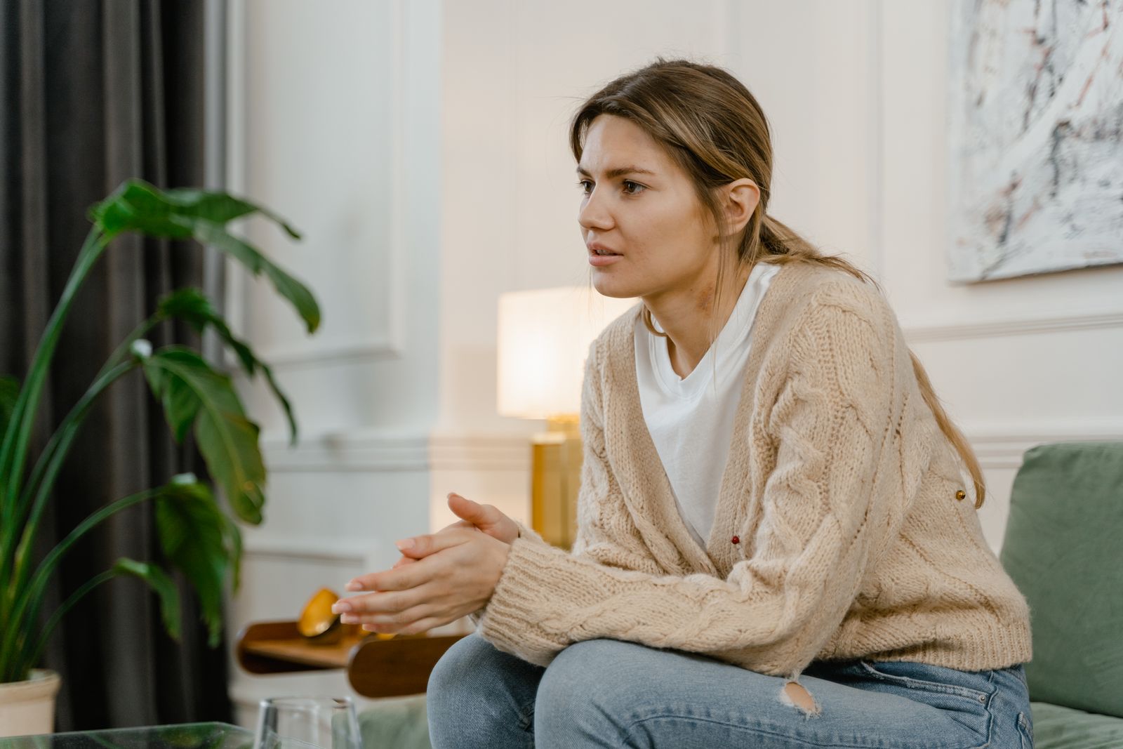 Woman in a casual setting appears deep in thought while sitting on a couch at home.