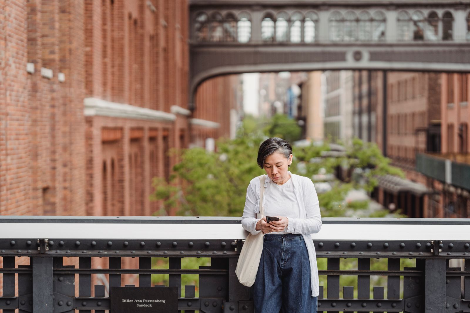 A woman uses her smartphone while leaning on a bridge in an urban setting, depicting connectivity and modern lifestyle.