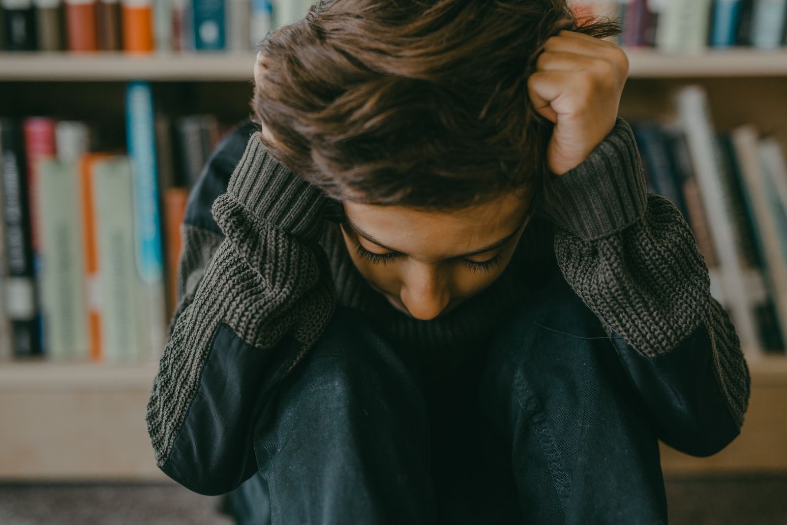 A young person sitting in a thoughtful, introspective pose in a library setting.