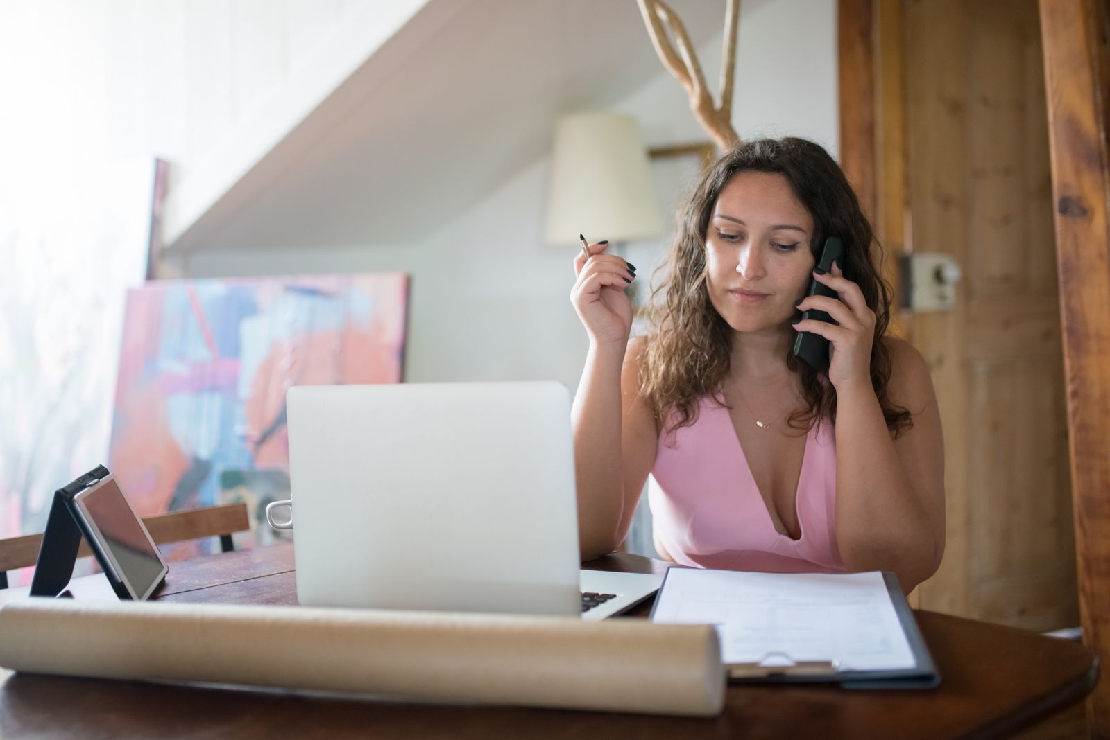 Young woman multitasking with phone and laptop in a cozy home office setting.
