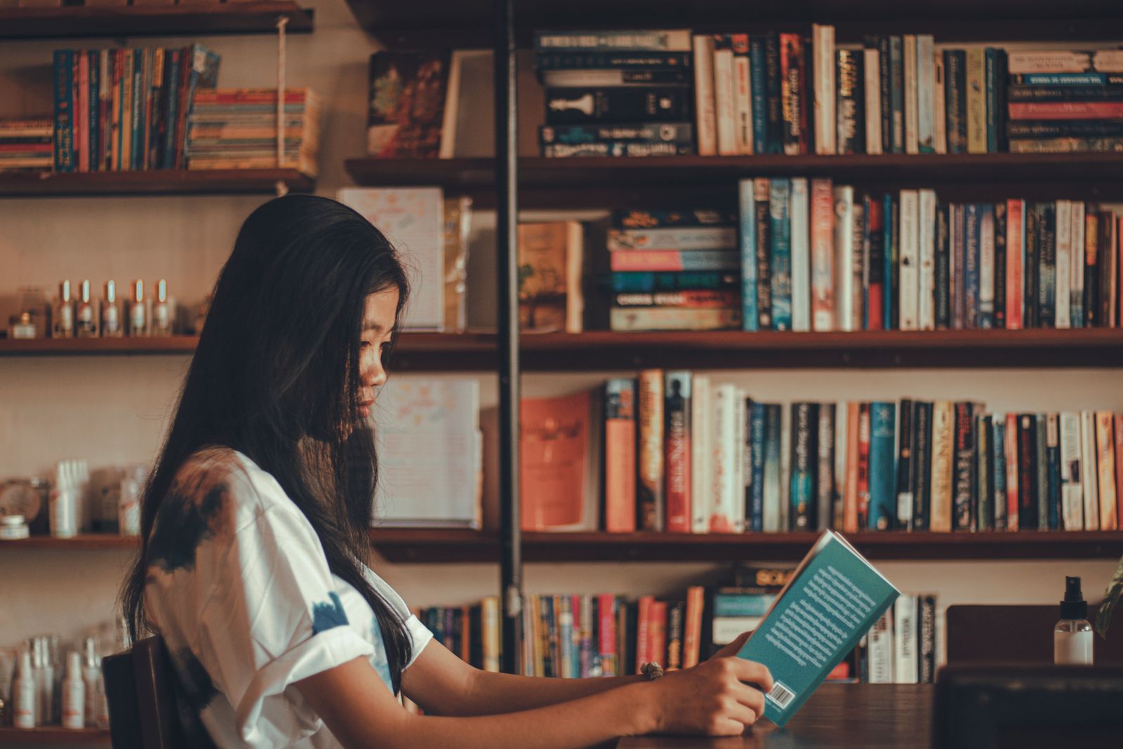 A young woman reads a book in a comfortable library with shelves full of books, offering a serene setting for relaxation.