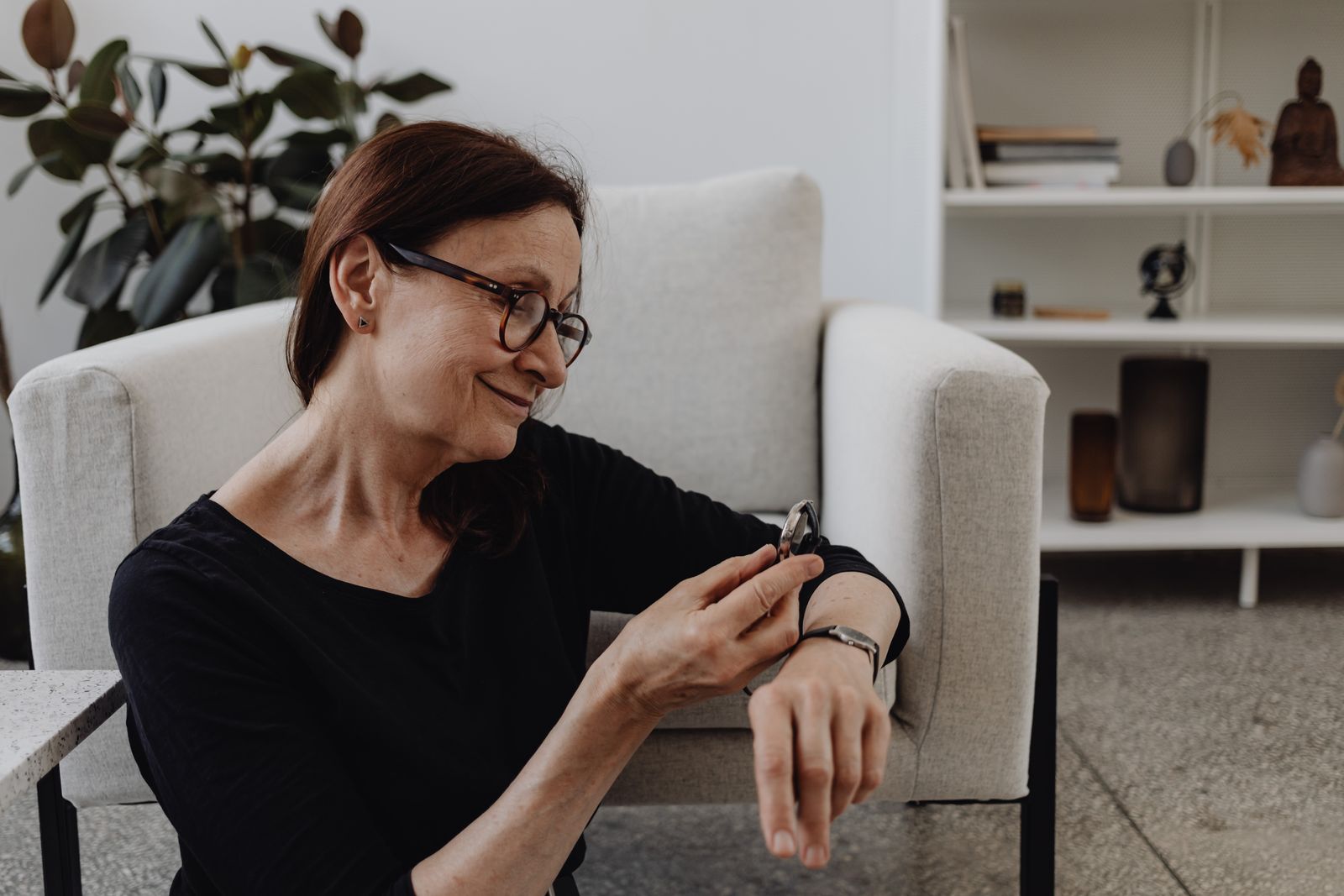 A woman smiles while checking her wristwatch in a comfortable living room setting.
