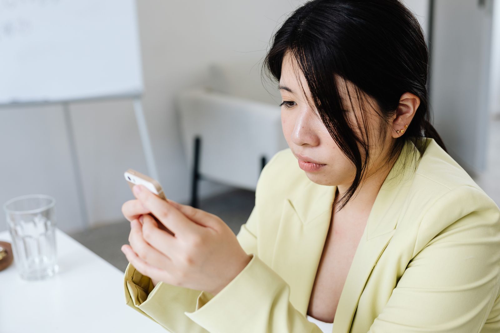 Focused woman in yellow blazer texting on smartphone at the office table.