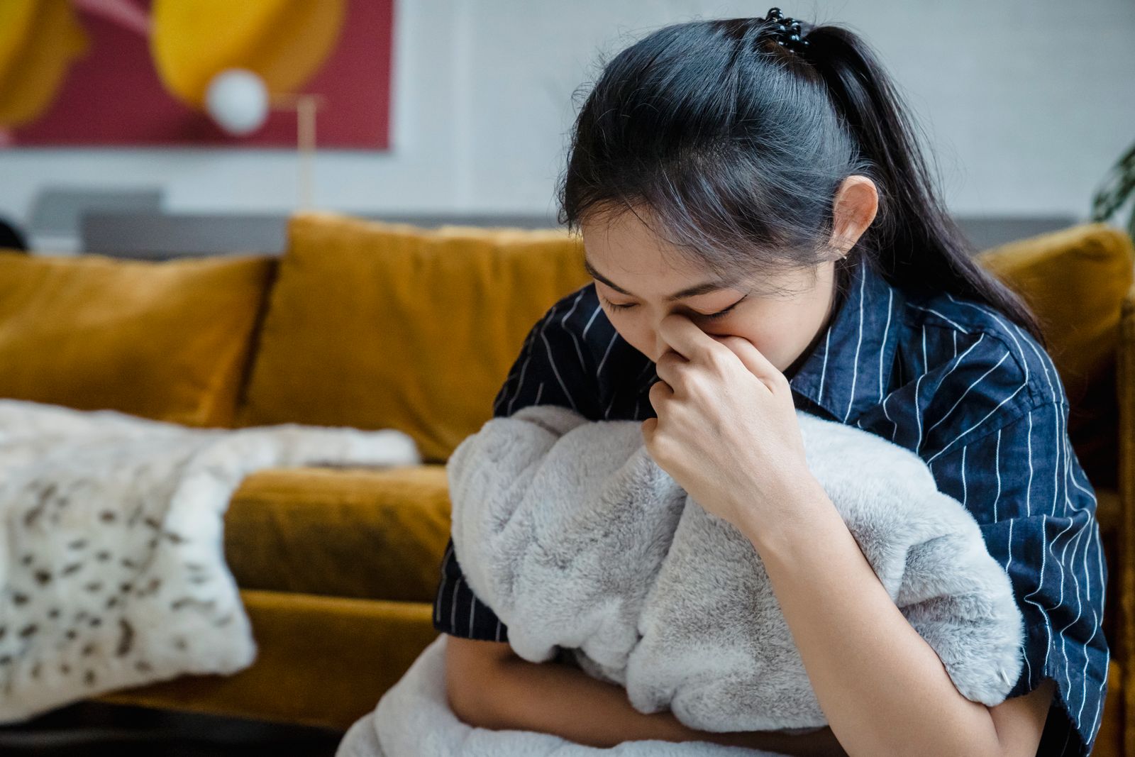A woman sitting indoors, holding a blanket, conveying emotions of stress and contemplation.