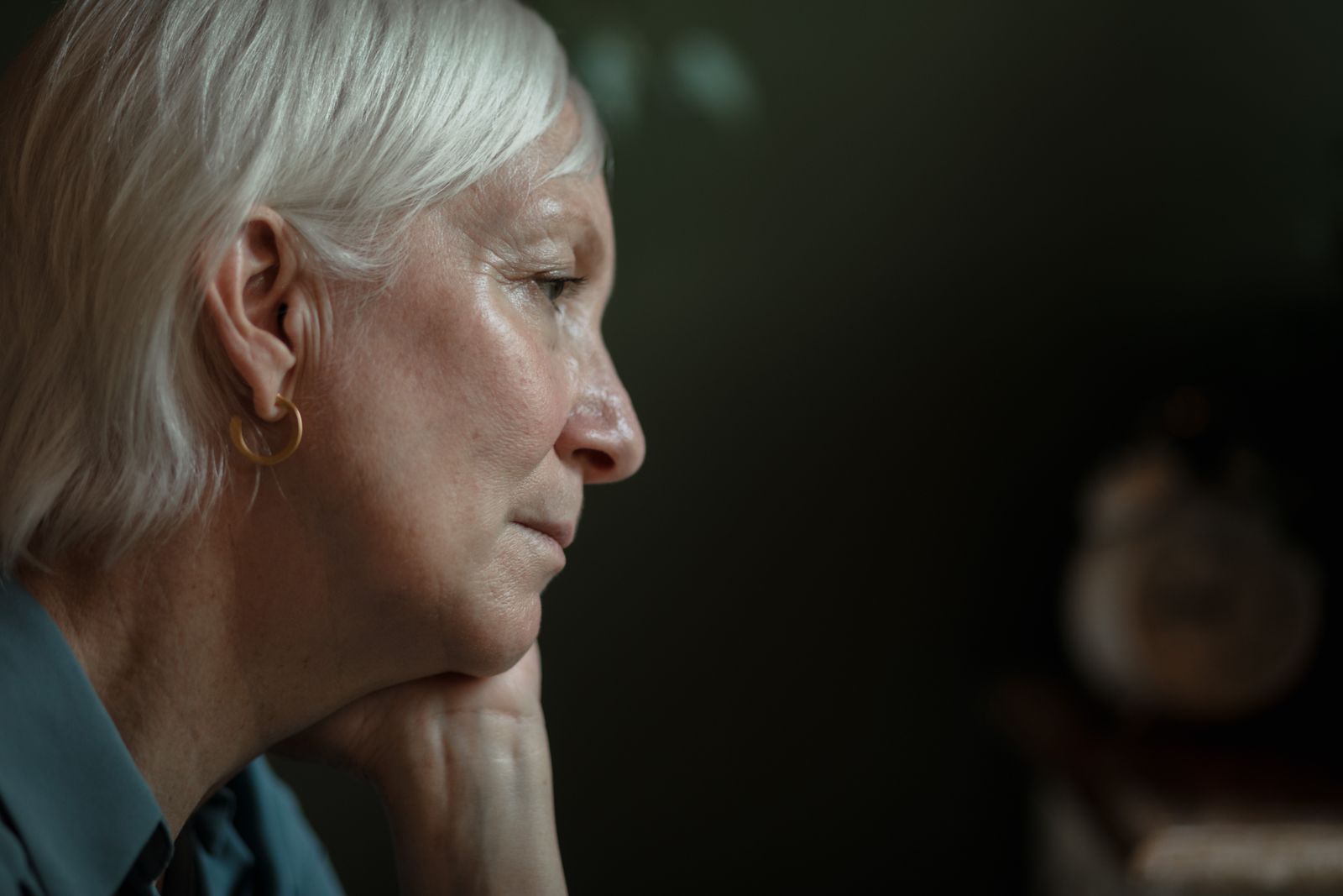 A thoughtful senior woman with white hair in a side profile view, lost in thought.