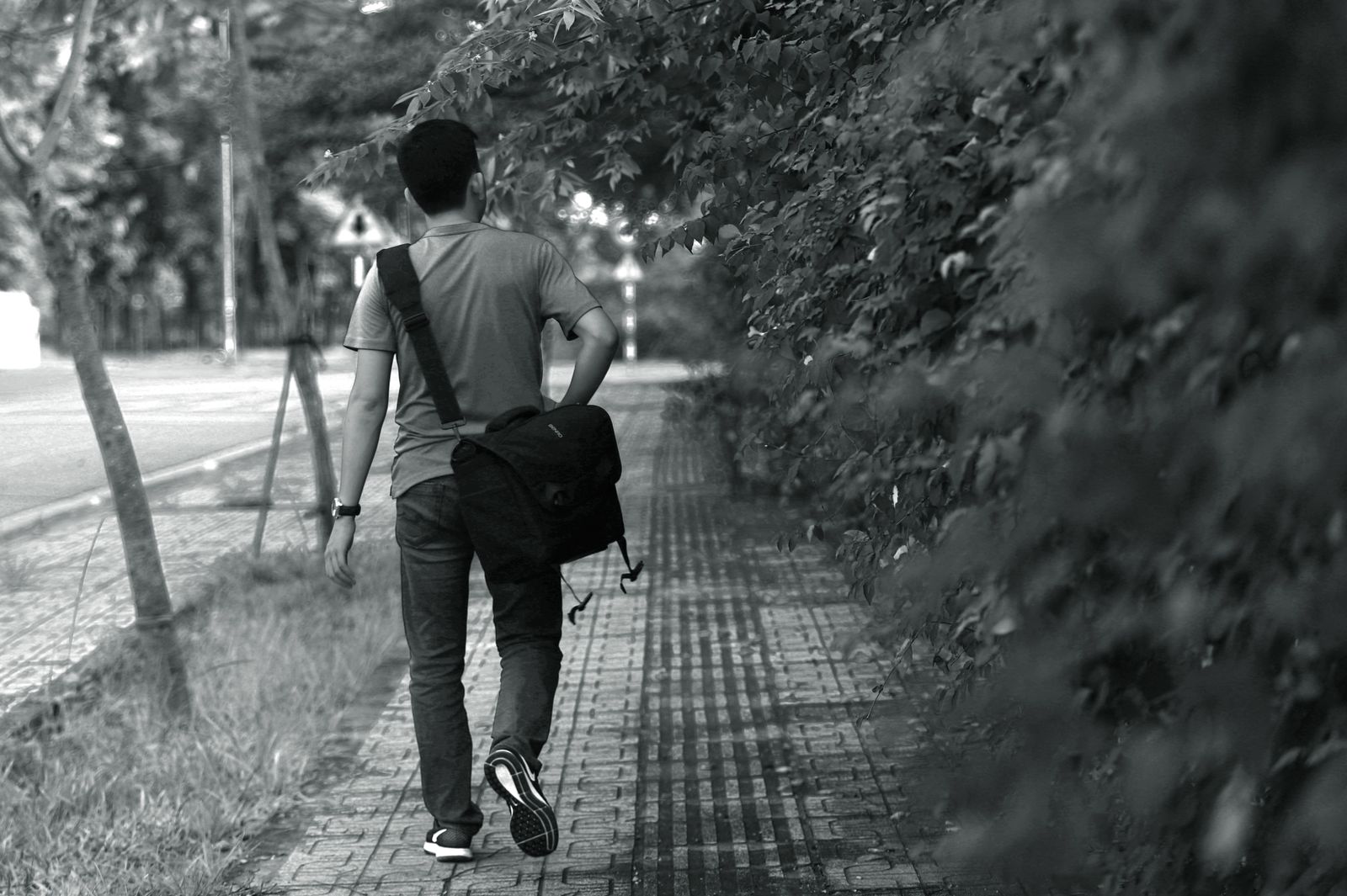 Black and white photo of man walking on sidewalk with messenger bag.