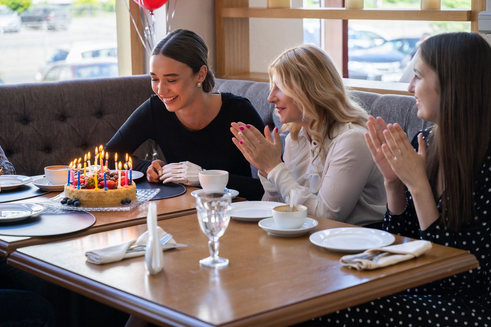 Friends celebrating a birthday with cake and laughter in a cozy café setting.