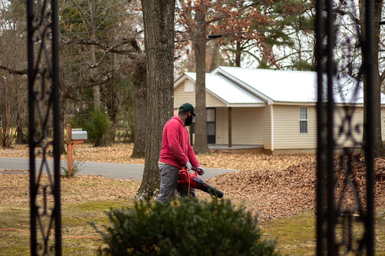 A man cleans fallen leaves with a blower in a residential neighborhood during autumn.