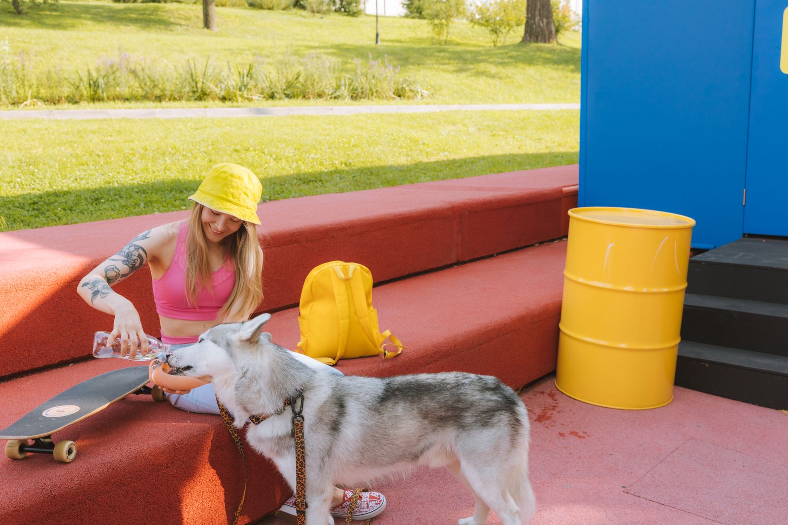 A woman enjoys a sunny day at the park with her Siberian Husky and skateboard.