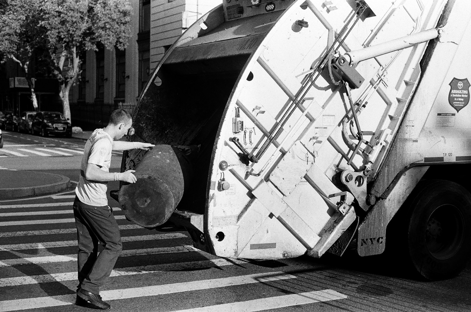 a black and white photo of a man unloading a garbage truck