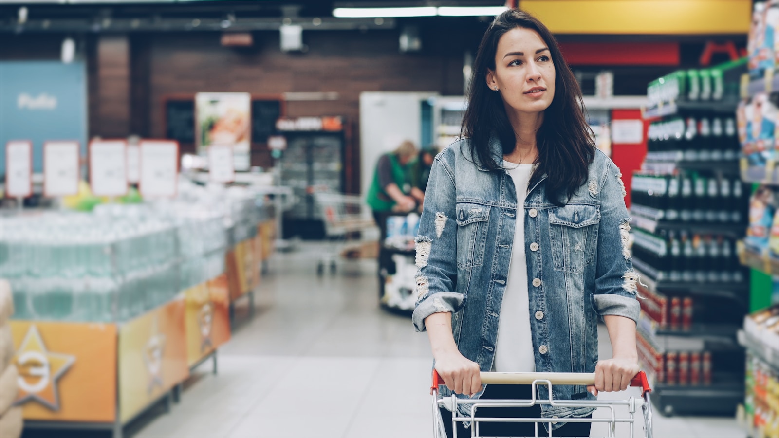 Woman shops in a supermarket, pushing a cart.