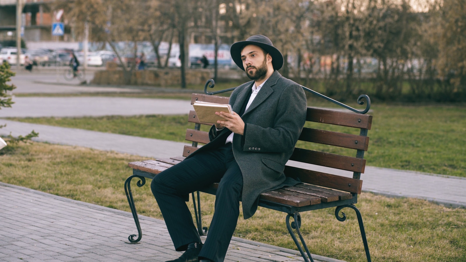 Man in hat reads book on park bench