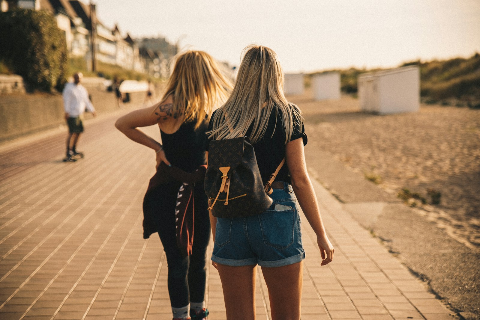 woman in black t-shirt and blue denim shorts walking on sidewalk during daytime