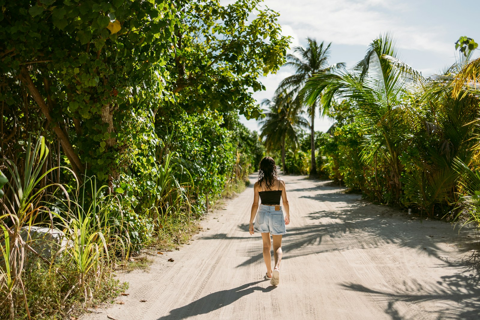 Woman walking down a dirt road surrounded by lush greenery.