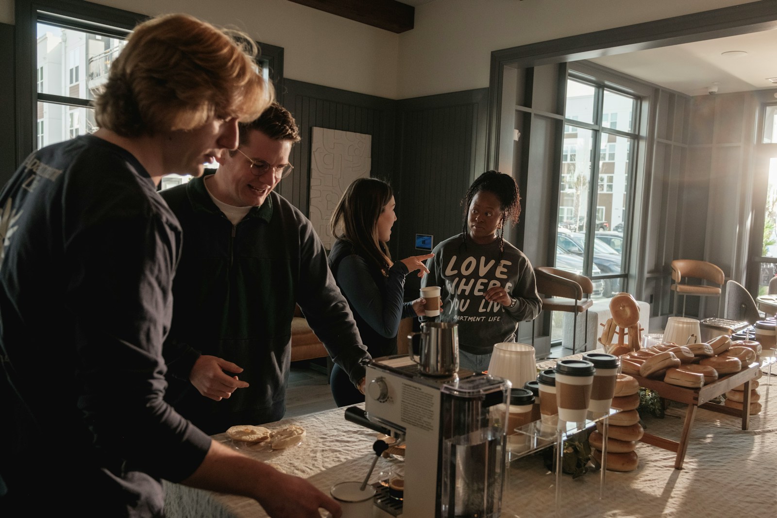 People gathered around a coffee machine in a kitchen.