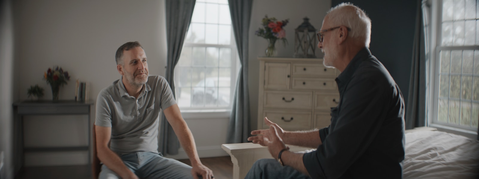 Two men talking in a sunlit room.