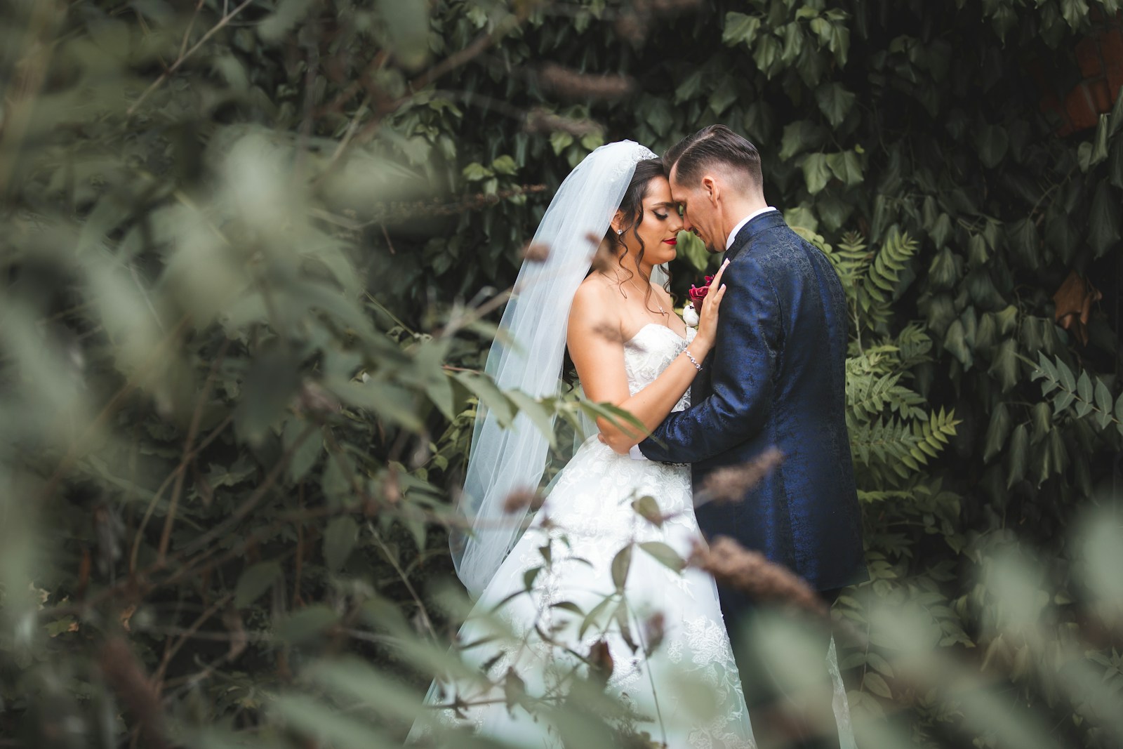 Bride and groom embracing in lush green foliage