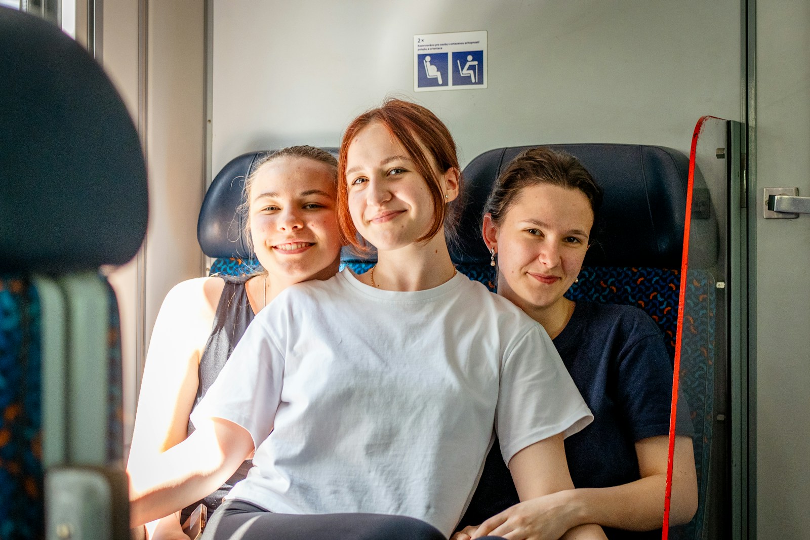 Three young women smiling while sitting on a train.