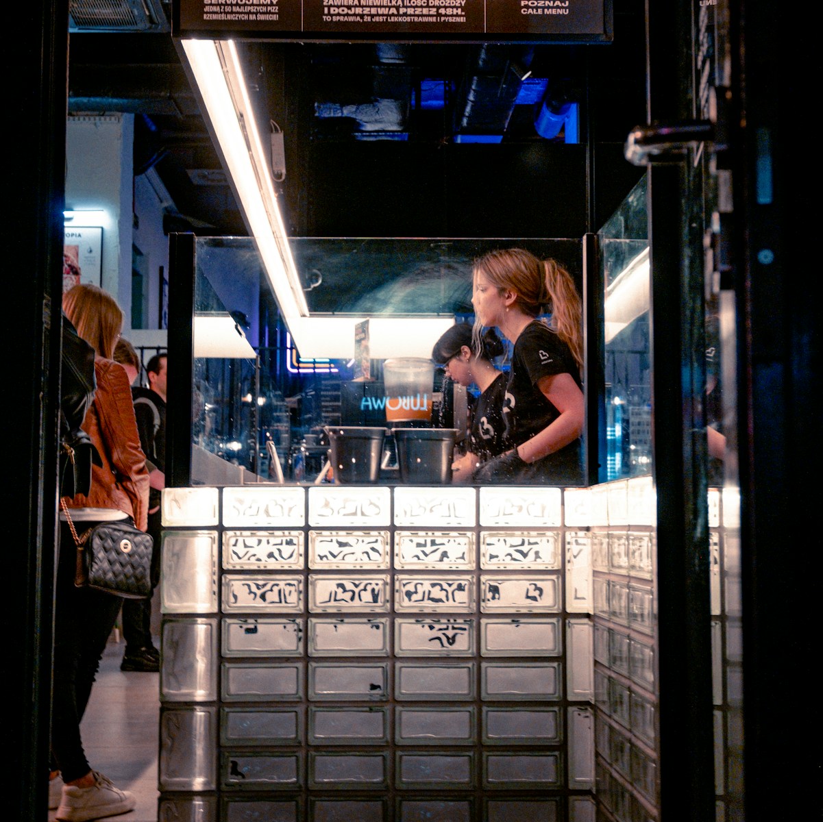 Woman serving at a brightly lit glass block counter.