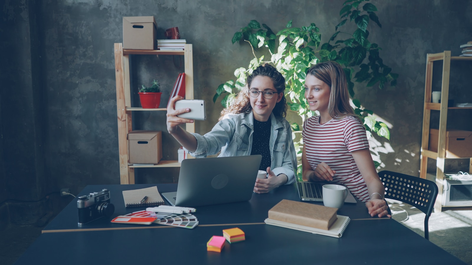 Two women take a selfie at a desk.