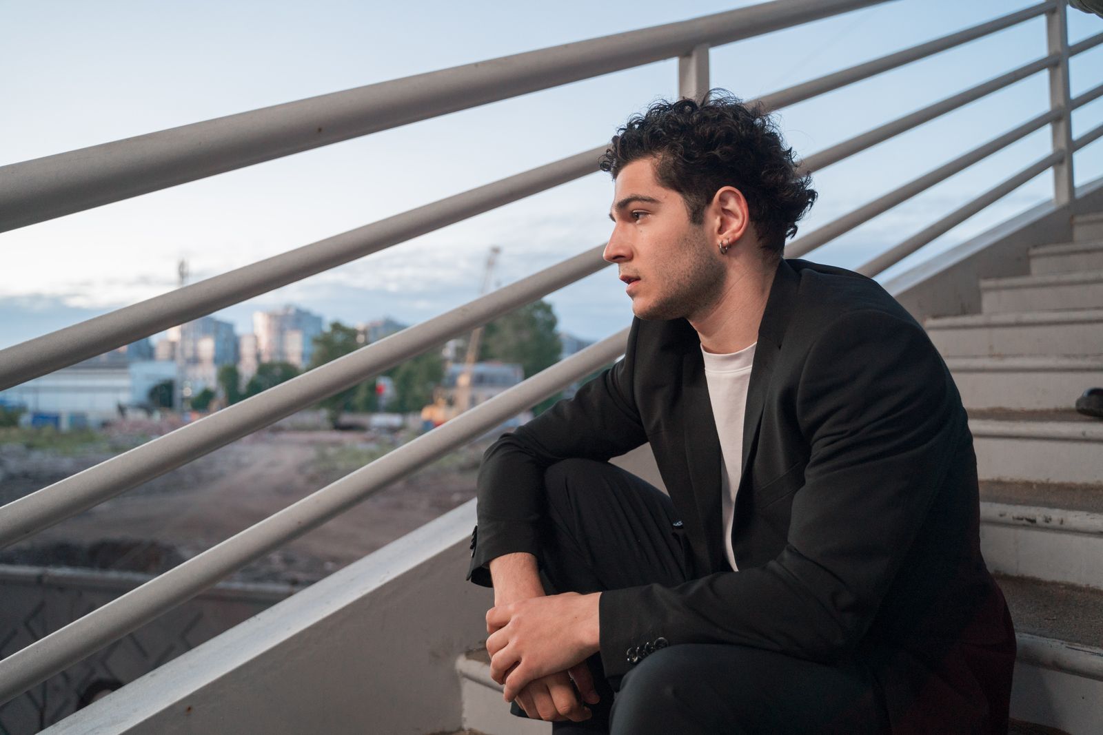A young man in a blazer sitting on stairs outdoors during the day.