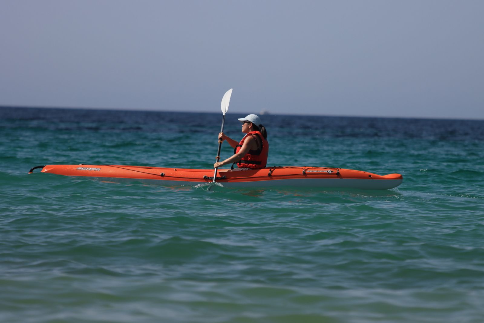 Woman kayaking in vibrant orange kayak on open ocean on a sunny summer day.