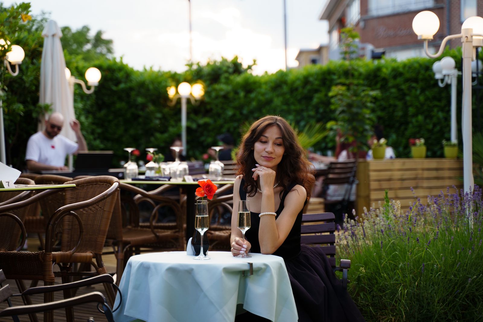 A young woman in a black dress enjoys champagne at an outdoor patio, creating a romantic dining atmosphere.
