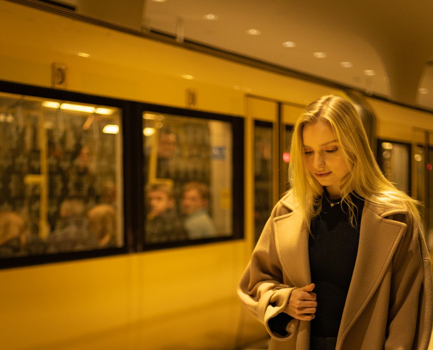 Stylish young woman in a beige coat posing at a train station.