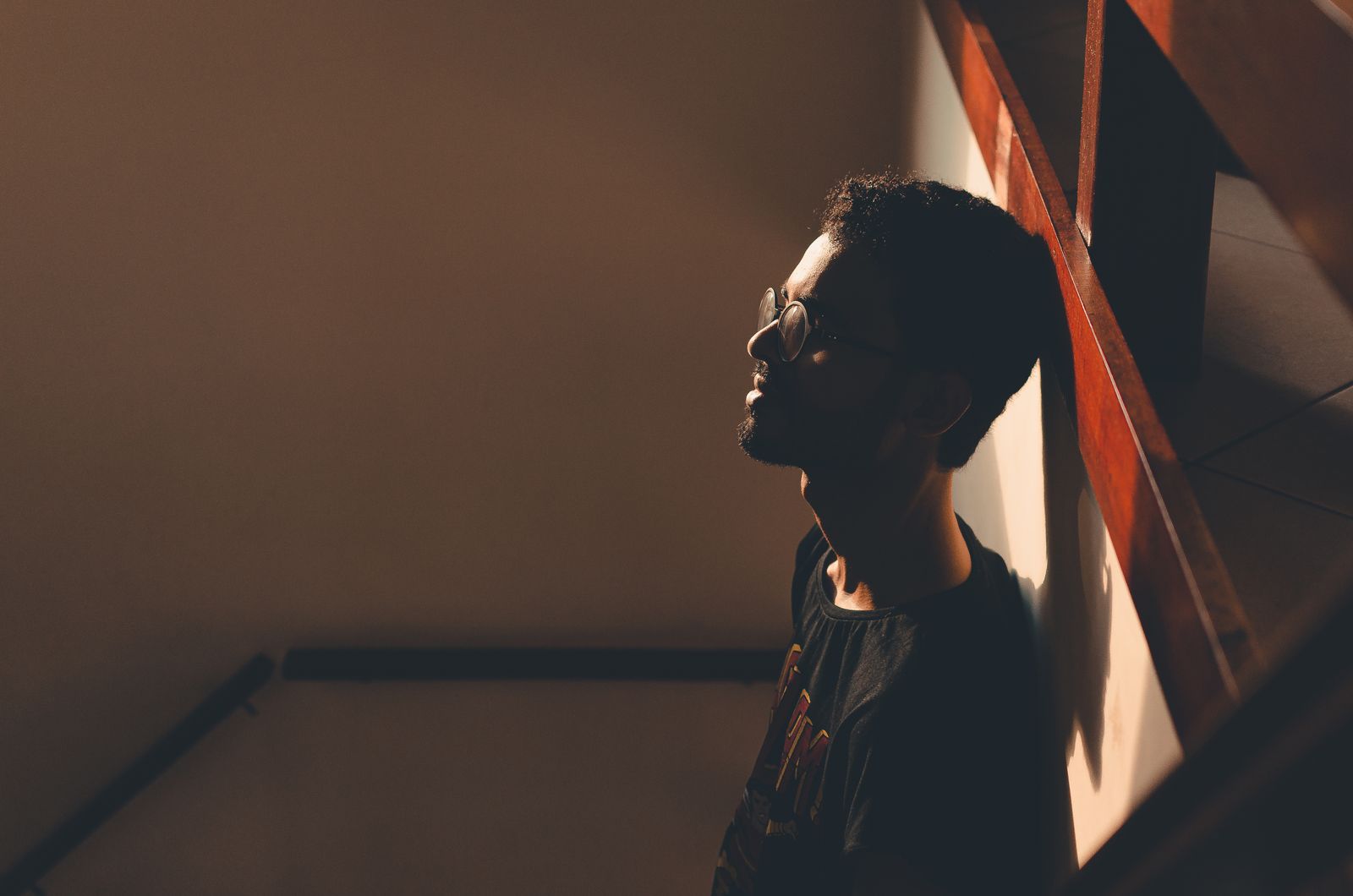 From above side view of young bearded man in eyeglasses leaning on wall at home