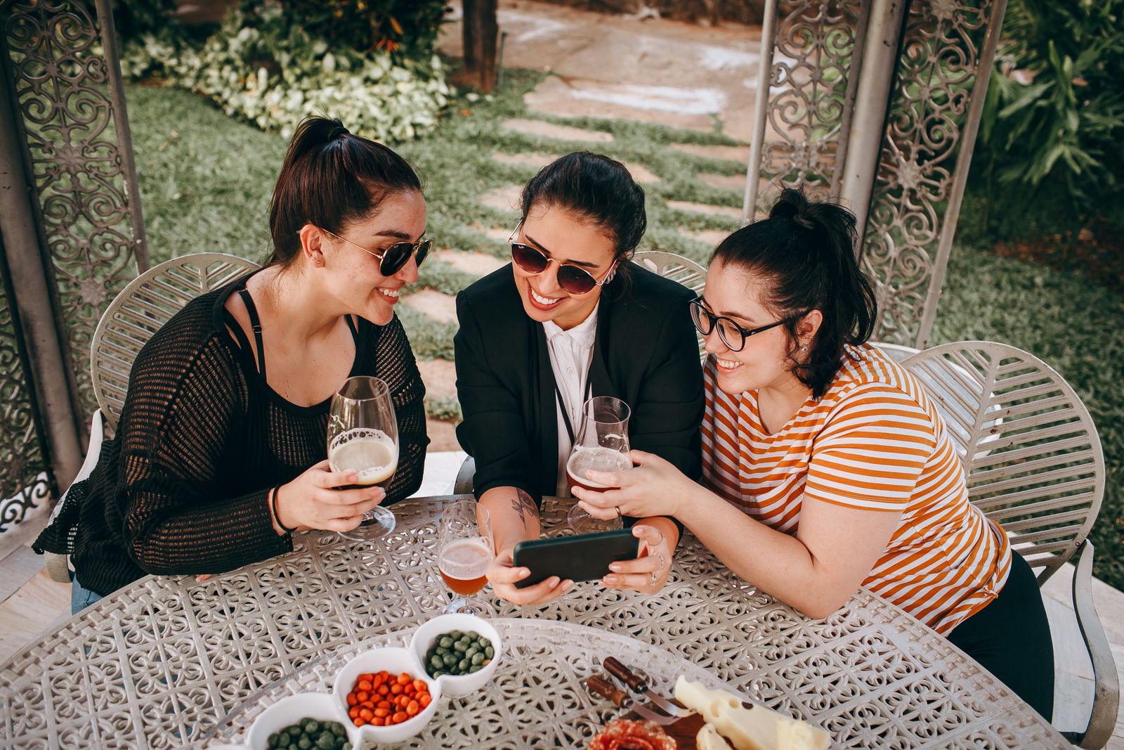 Three women sitting outdoors, sharing moments over drinks. Captured in a garden setting.