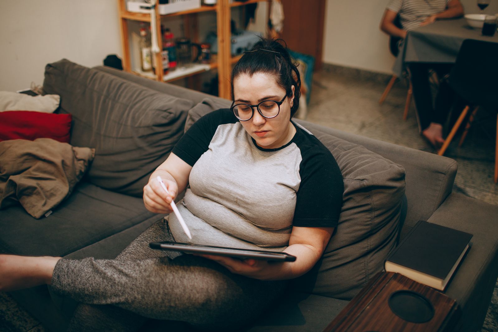 Woman relaxing on a couch while using a digital tablet stylus, ideal for remote work or casual browsing.