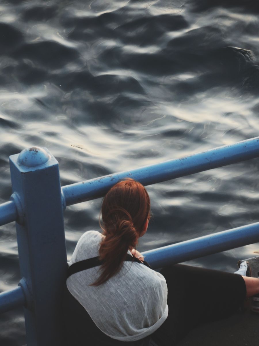 A woman sits by the water's edge reflecting during twilight.