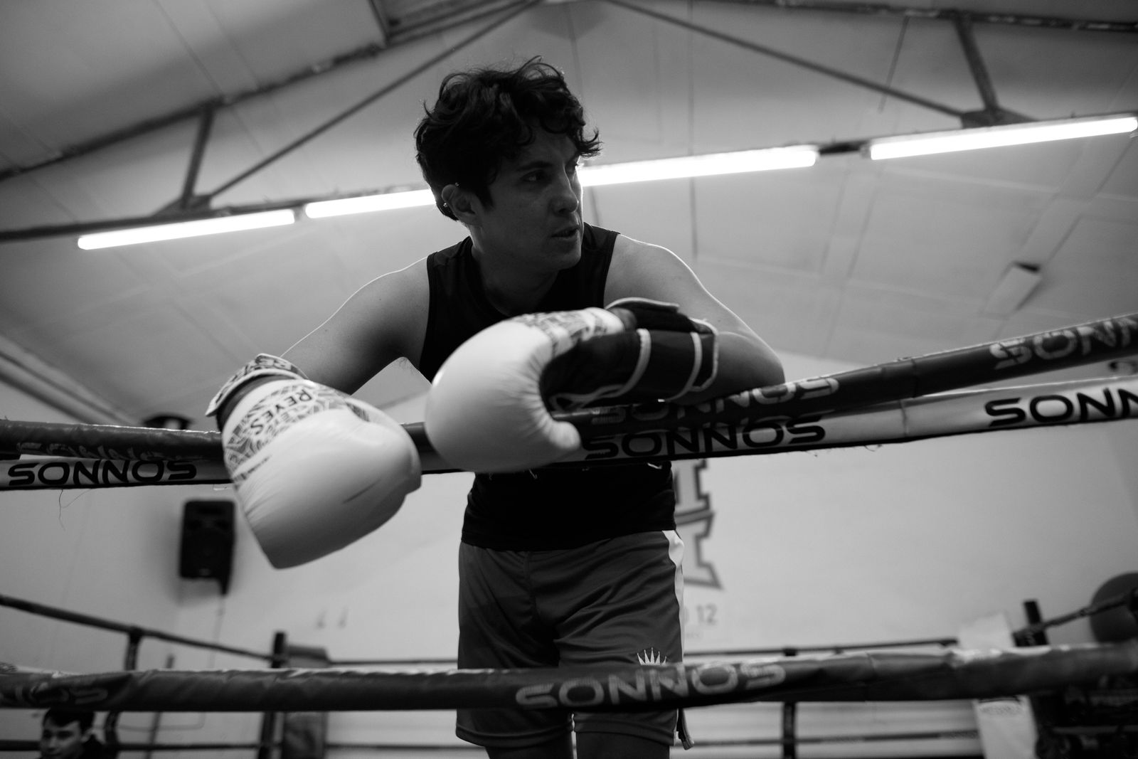A focused boxer wearing gloves leaning on ropes in a Buenos Aires gym.
