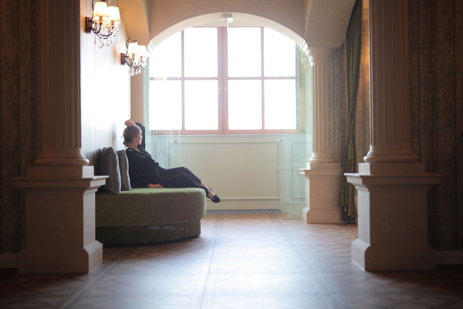 A woman in a stylish hallway, seated near a large window, illuminated by natural light.