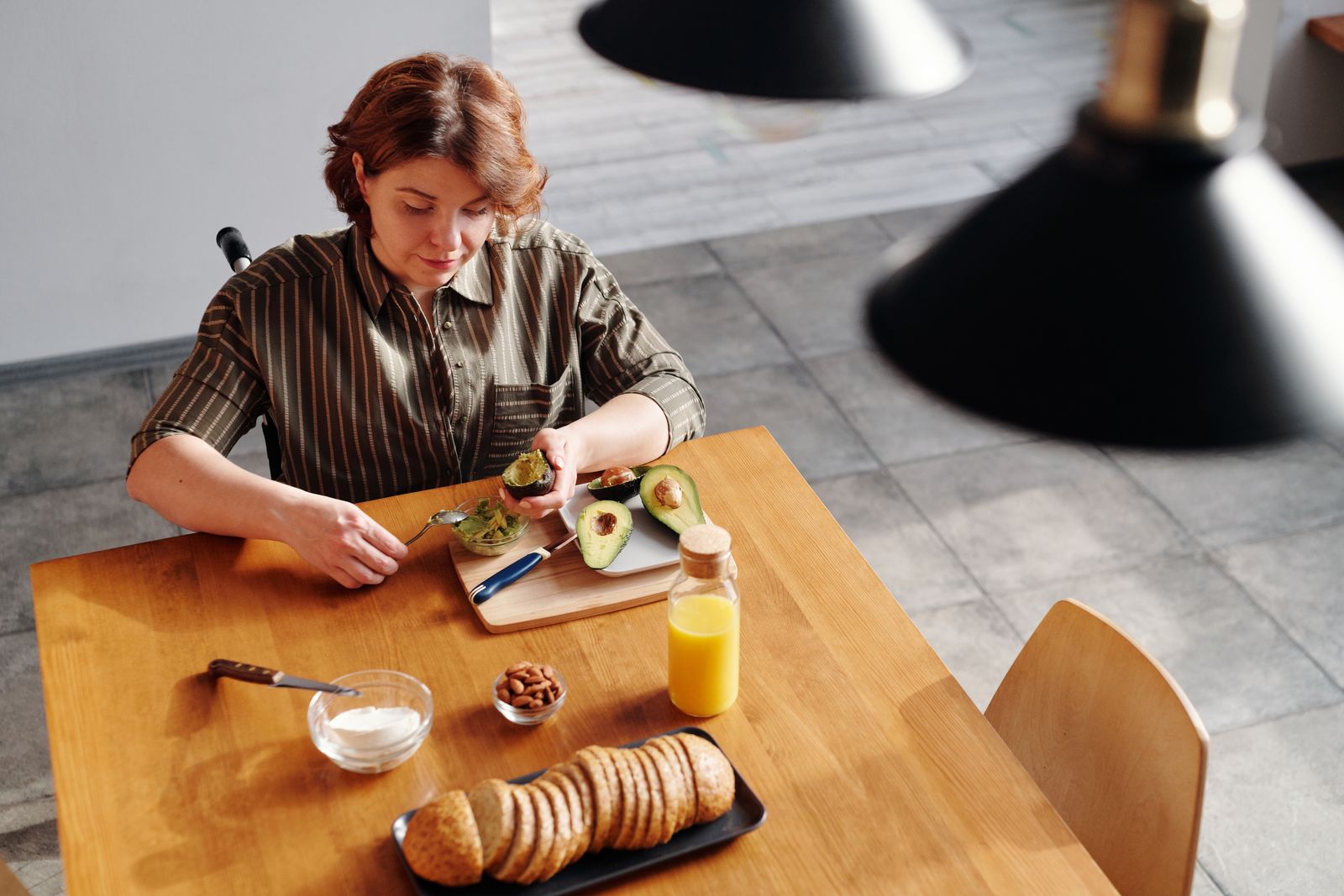 Woman prepares a nutritious breakfast with avocado and orange juice at home.