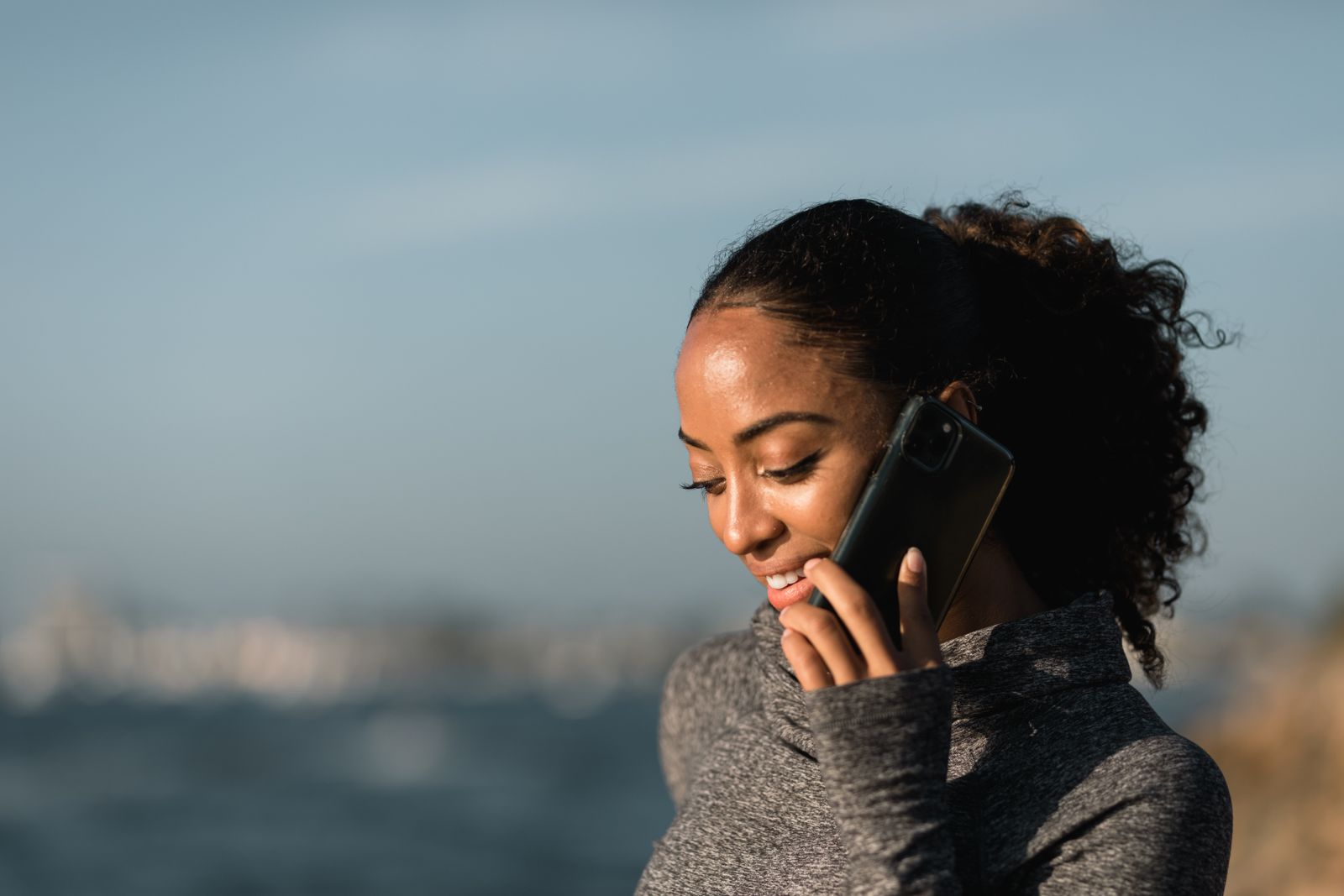 Young woman smiling during a phone call by the sea on a sunny day.