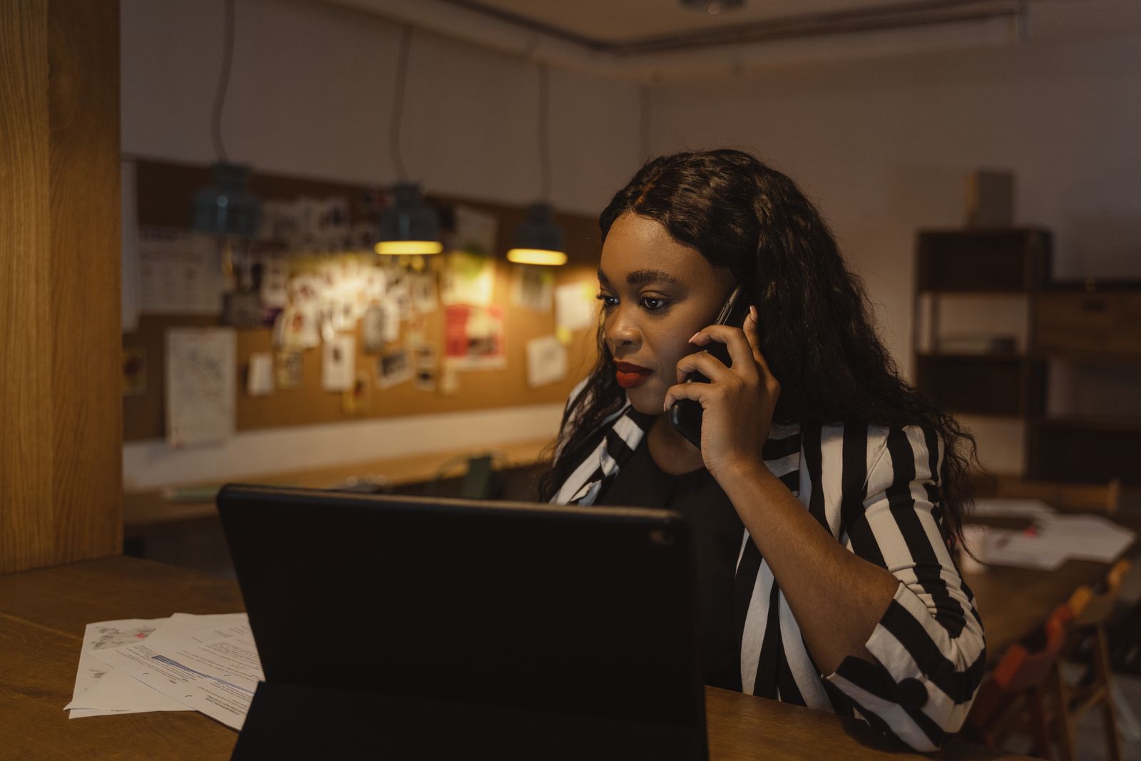 African American woman in a striped blazer making a phone call in a modern office.