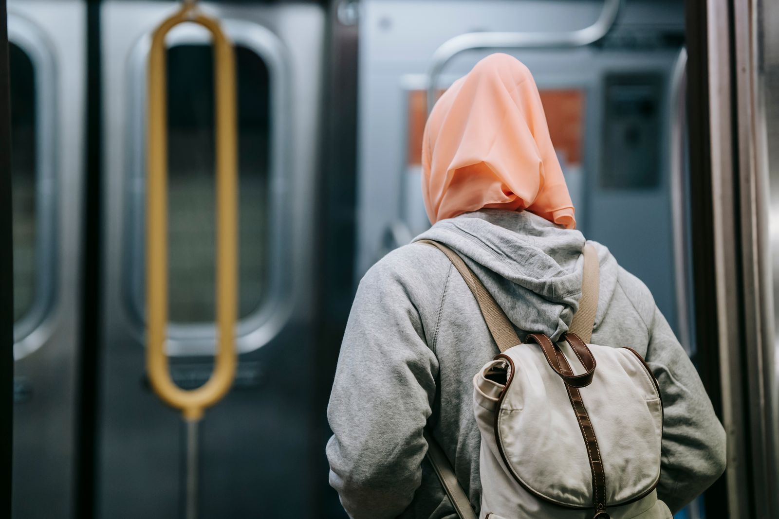 Back view of Muslim female in casual wear and traditional headscarf and with backpack in underground train