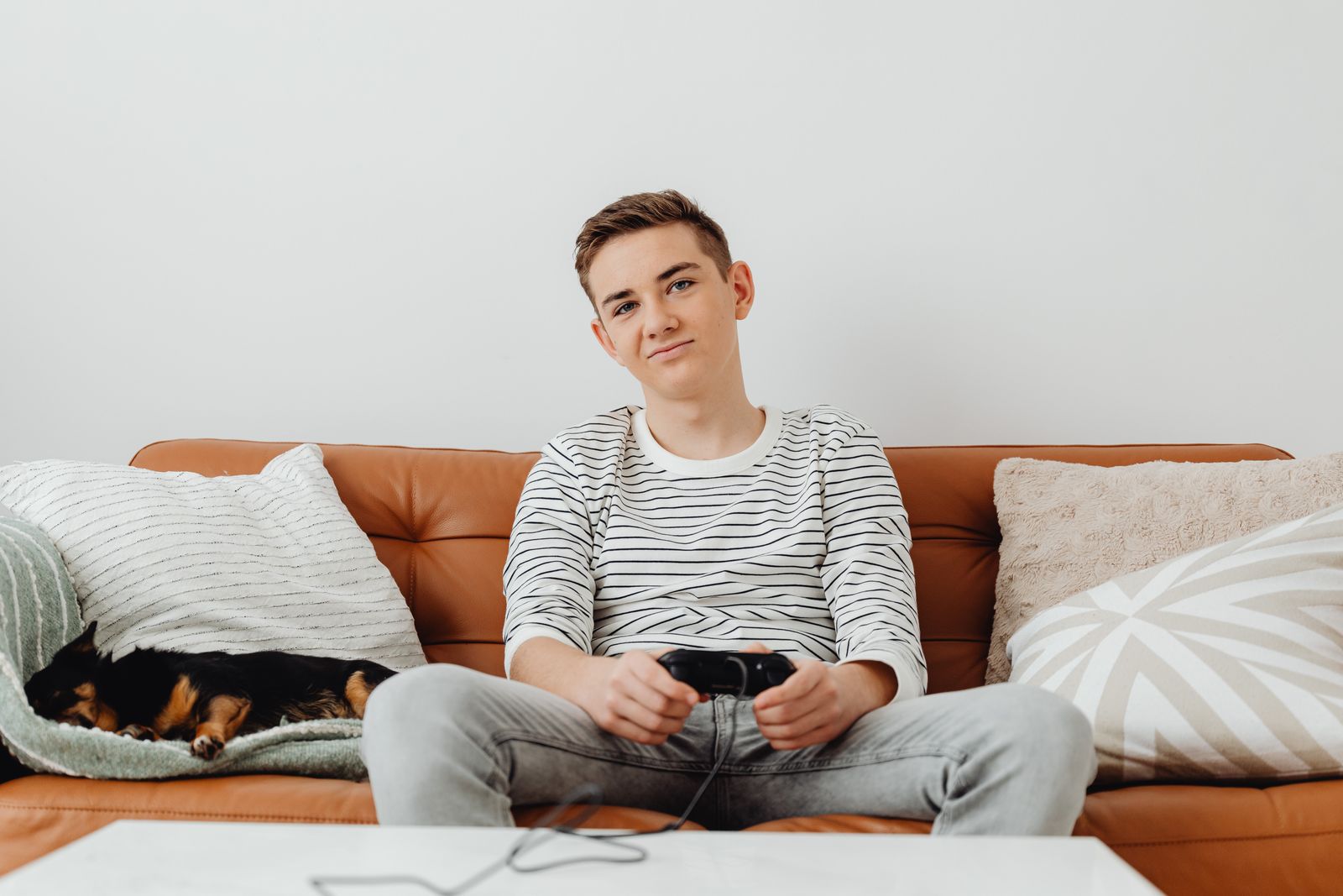 Teenager playing video games on the sofa with a dog sleeping beside him.