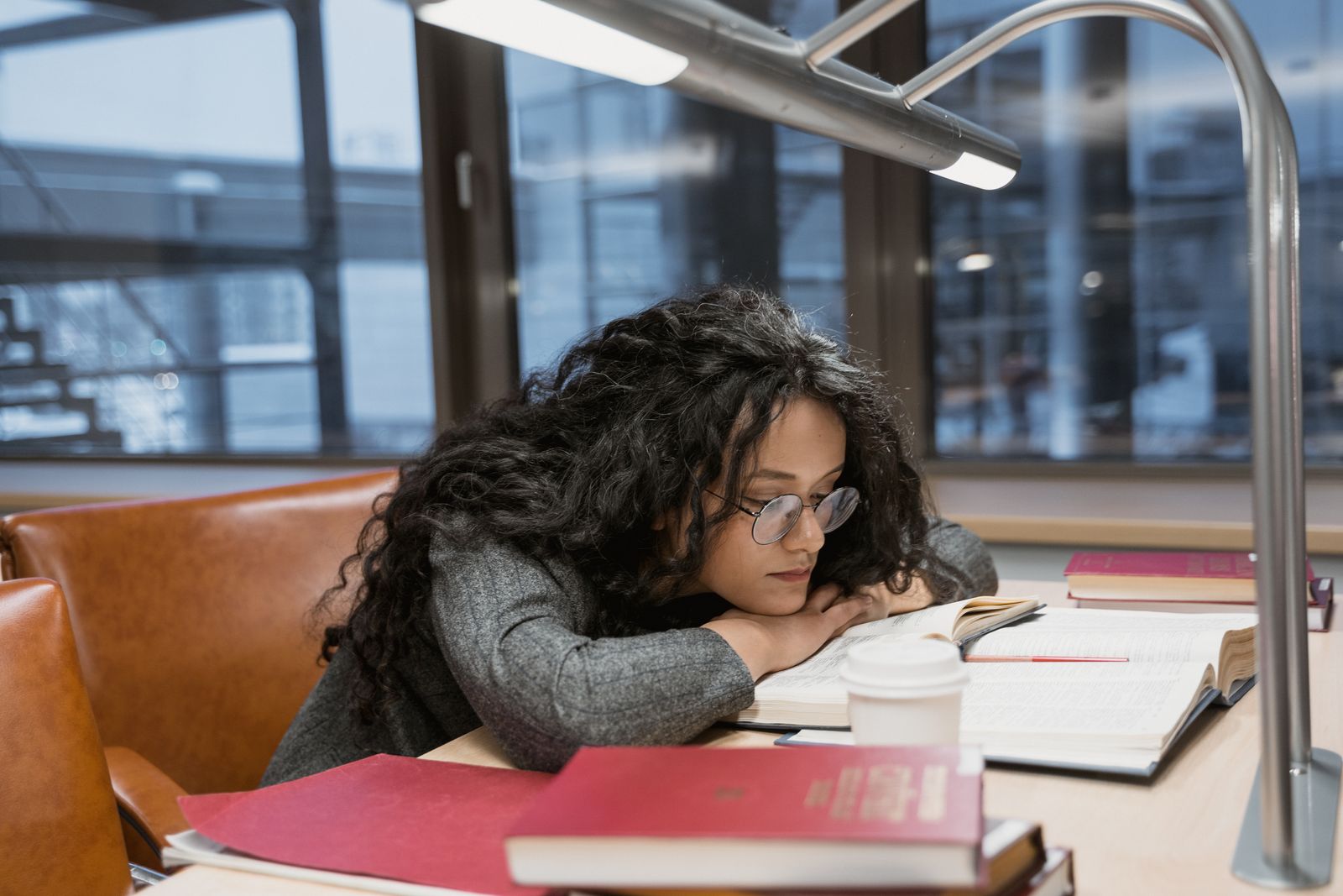 Tired young woman studying at a library desk, surrounded by books and notes.