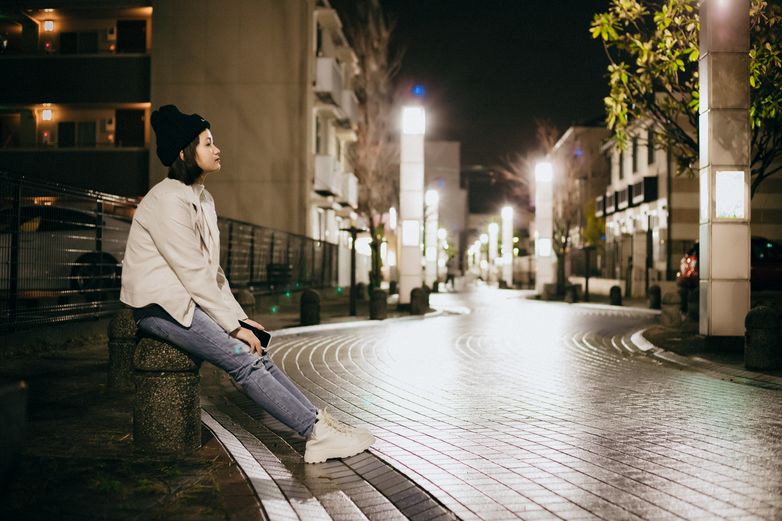 Woman sitting on a bench in an illuminated urban street at night, reflecting a peaceful moment.