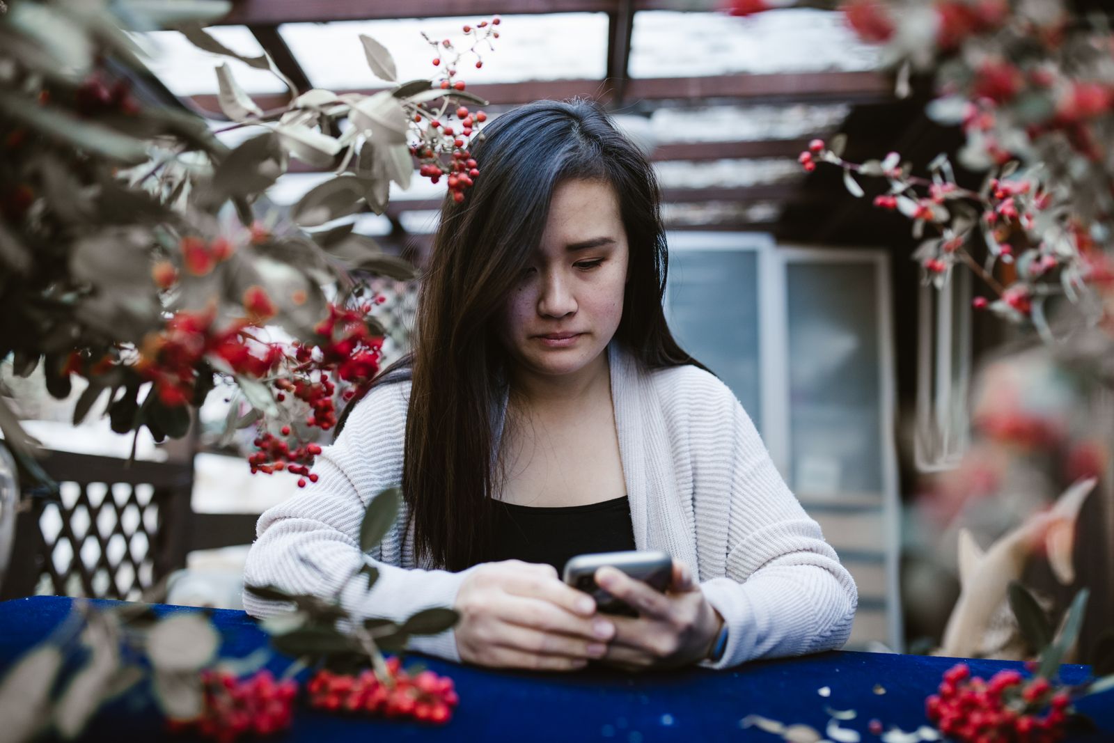 A contemplative woman using her smartphone outdoors surrounded by foliage.