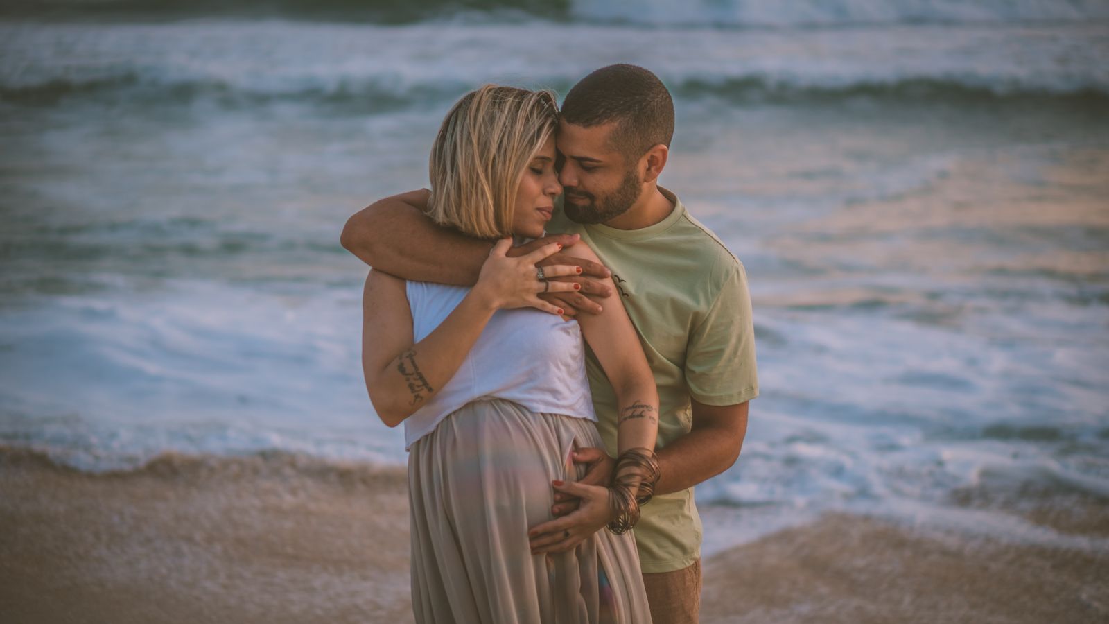 A loving couple embraces on a serene beach, highlighting intimacy and expectation.