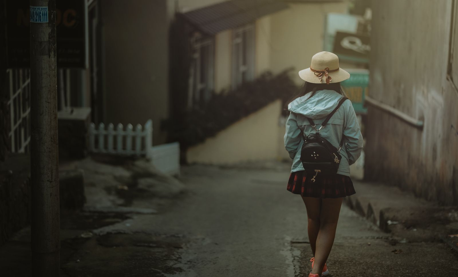 A young woman with a backpack strolls through a quiet urban alleyway in daylight.