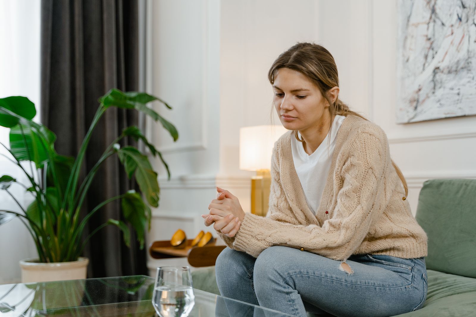 Woman sitting on sofa in living room, looking contemplative and relaxed.