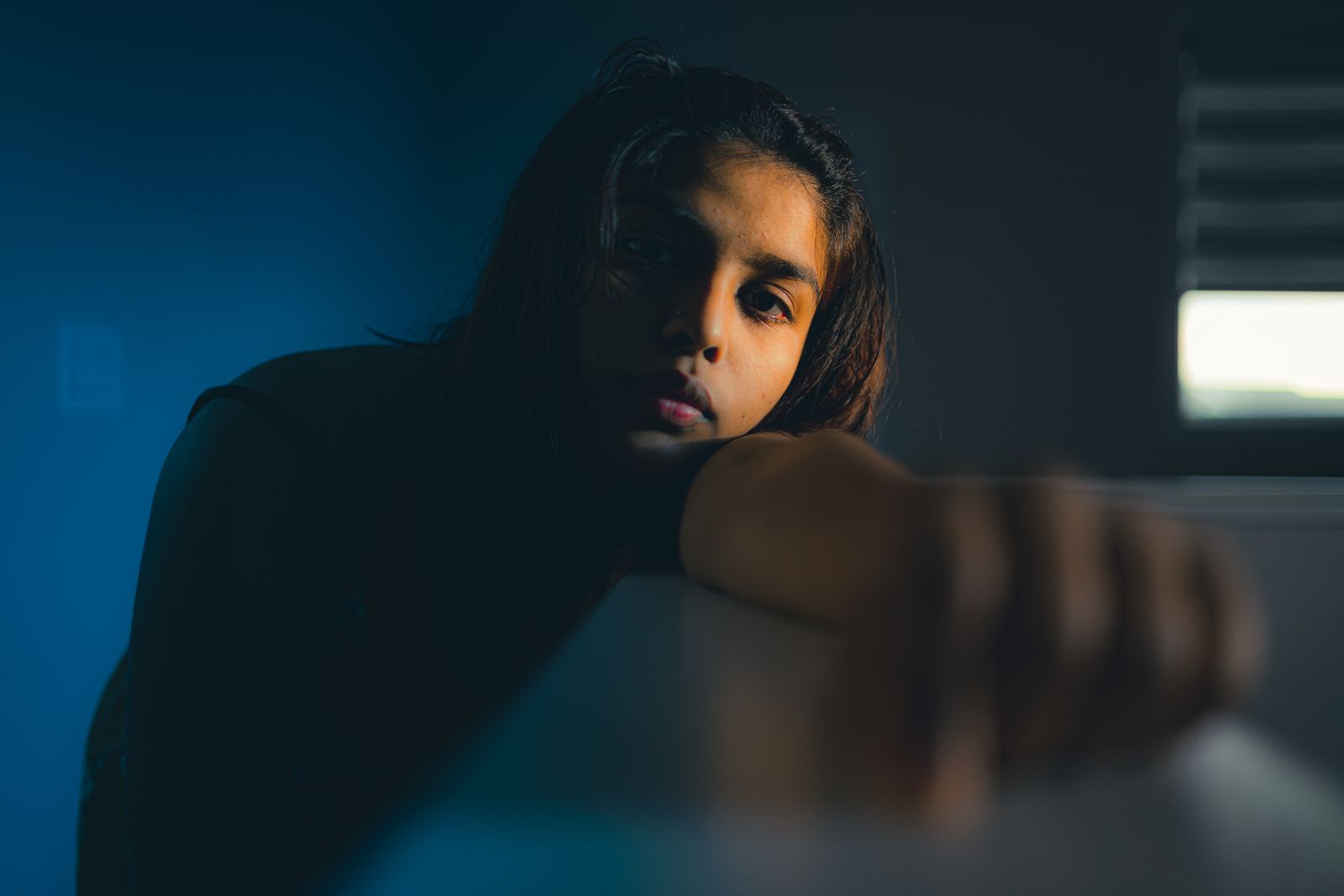 A young woman in a contemplative pose with dramatic lighting indoors.